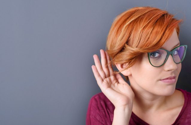 Frau mit Brille hält Hand ans Ohr zum besseren Hören