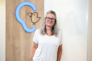 Mitarbeiterin Astrid Harringer steht vor einer Wand mit Bagus-Logo