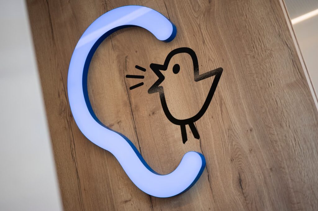 Leuchtendes Logo von Bagus mit stilisiertem Ohr und Vogel auf Holzfläche