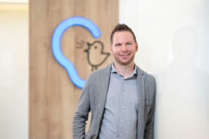 Mitarbeiter Johannes Graf steht vor einer Wand mit Bagus-Logo