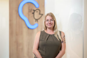 Mitarbeiterin Melanie Sober steht vor einer Wand mit Bagus-Logo