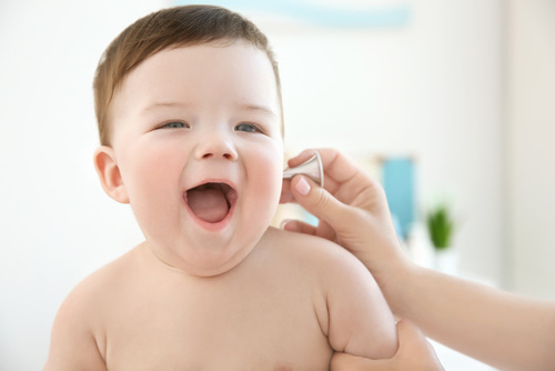 Lächelndes Baby beim Hörtest mit kleinem Messgerät am Ohr