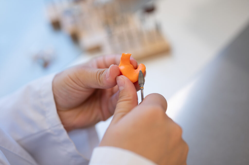 Hände eines Akustikers formen ein maßgefertigtes Ohrpassstück